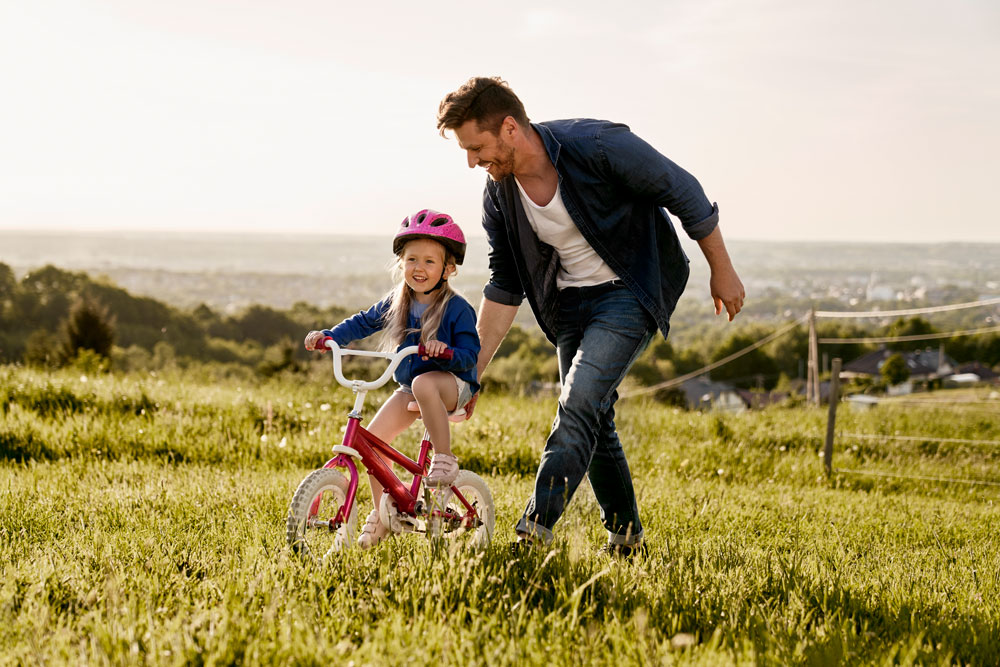 homem empurrando criança andando de bicicleta em um campo aberto